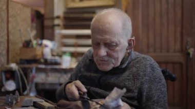 Senior gray haired male master in a wheelchair is working at his workshop sharpening japanese swords blade