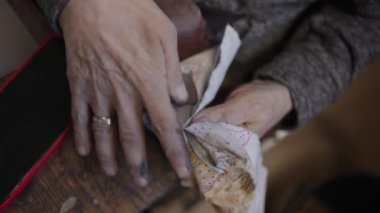 Senior gray haired male master in a wheelchair is working at his workshop sharpening japanese swords blade
