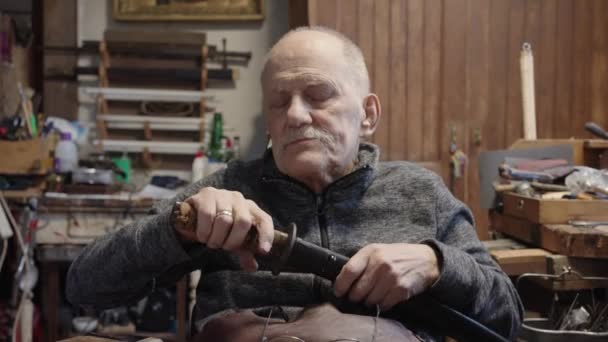 車椅子のシニアグレーの髪の男性マスターは 日本刀を復元する彼のワークショップで働いています — ストック動画
