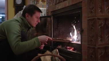 Evdeki şömineye odun koyan bir adam ateş yakıyor.
