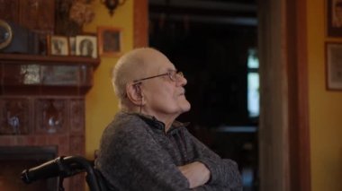Tekerlekli sandalyede oturan yaşlı bir adam şöminenin yanında televizyon izliyor.