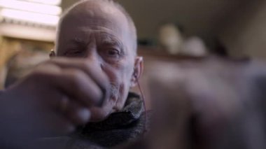Senior gray haired male master in a wheelchair is working at his workshop sharpening japanese swords blade