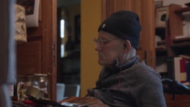 Tekerlekli sandalyedeki kıdemli ressam bir stüdyoda tuvale yağlı boya bir resim çizer.