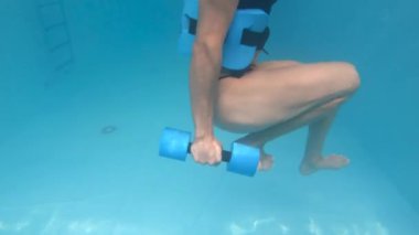 Genç bir kadın havuzda, su altında spor yapıyor.