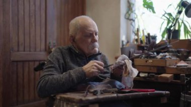 Senior gray haired male master in a wheelchair is working at his workshop sharpening japanese swords blade