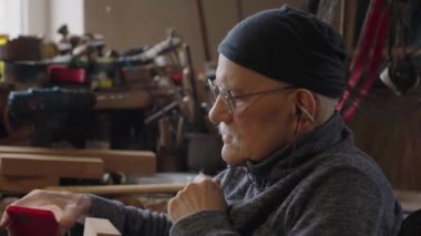 Tekerlekli sandalyedeki yaşlı erkek usta atölyesinde mobilyaları restore ediyor.