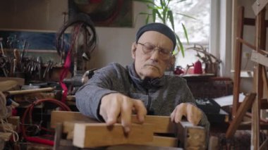 Tekerlekli sandalyedeki yaşlı erkek usta atölyesinde mobilyaları restore ediyor.