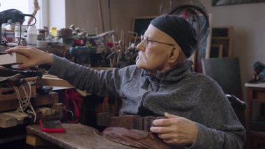 Tekerlekli sandalyedeki yaşlı erkek usta atölyesinde mobilyaları restore ediyor.