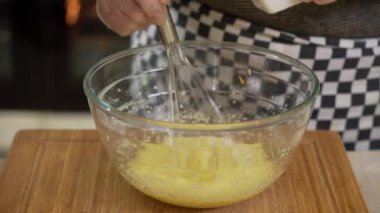 Şef yumurtaları sütle karıştırıyor ve un hamur çırpıyor.