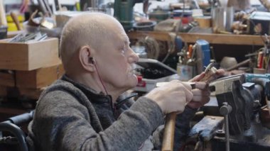 Tekerlekli sandalyedeki kıdemli yaşlı kuyumcu bir atölyede çalışıyor.