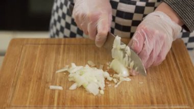 Şef kesme tahtasının üzerinde bıçakla soğan doğruyor.