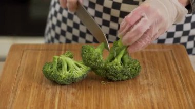 Şef, tahta bir tahtanın üzerinde brokoli kesip soyuyor.