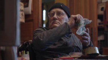 Tekerlekli sandalyedeki kıdemli ressam bir stüdyoda tuvale yağlı boya bir resim çizer.