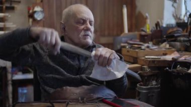 Senior gray haired male master in a wheelchair is working at his workshop sharpening japanese swords blade