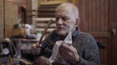 Senior gray haired male master in a wheelchair is working at his workshop sharpening japanese swords blade