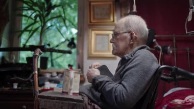 Tekerlekli sandalyedeki yaşlı bir adam yatak odasındaki yatağın yanında ilaç alıyor.