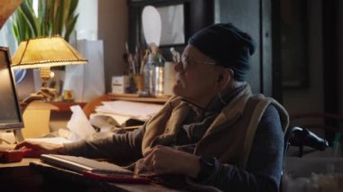 Kronik engelli yaşlı yetişkin tekerlekli sandalyede oturan bilgisayarla çalışıyor.