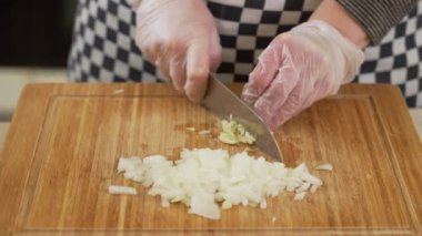 Şef soğan ve sarımsağı kesme tahtasında bıçakla doğruyor.