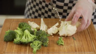 Şef, tahta bir tahtada brokoli ve karnabahar kesip soyuyor.