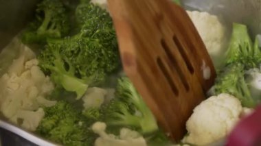 Şef tavada brokoli ve karnabahar pişiriyor.