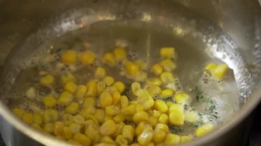 Şef tavada tereyağlı kırmızı biber ve tatlı mısır kızartıyor.