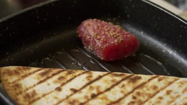 Şef ızgarada tortilla sandviçi ile ton balıklı biftek pişiriyor.