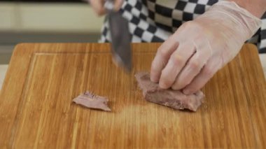 Şef, dilimlenmiş sığır dilini kesme tahtasıyla dilimliyor.