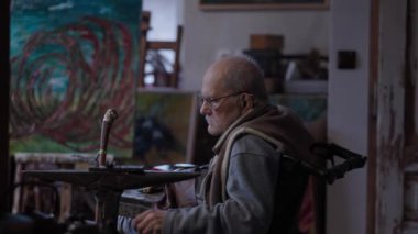 Senior elderly master jeweler in wheelchair works in a workshop with an anvil
