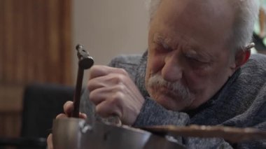 Tekerlekli sandalyede usta bir zanaatkar atölyesinde çalışıyor. Japon kılıcının ucuna çekiç ve keskiyle hormon resmi işliyor.