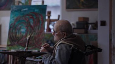 Senior elderly master jeweler in wheelchair works in a workshop with an anvil