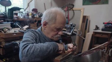 Tekerlekli sandalyede usta bir zanaatkar atölyesinde çalışıyor. Japon kılıcının ucuna çekiç ve keskiyle hormon resmi işliyor.
