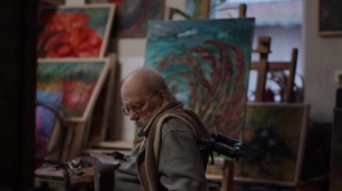 Senior elderly master jeweler in wheelchair works in a workshop with an anvil