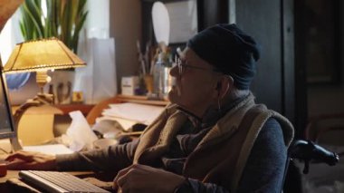 Kronik engelli yaşlı yetişkin tekerlekli sandalyede oturan bilgisayarla çalışıyor.