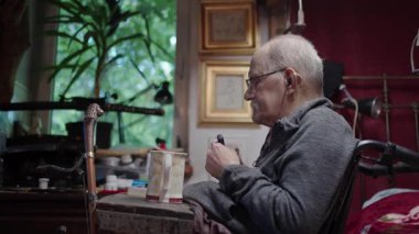 Tekerlekli sandalyedeki yaşlı bir adam yatak odasındaki yatağın yanında ilaç alıyor.