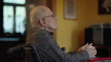 Tekerlekli sandalyede oturan yaşlı bir adam şöminenin yanında televizyon izliyor.