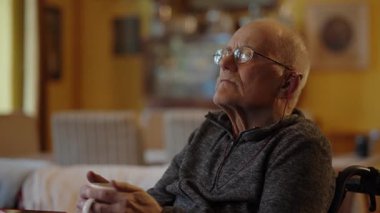 Tekerlekli sandalyede oturan yaşlı bir adam şöminenin yanında televizyon izliyor.