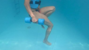 Genç bir kadın havuzda, su altında spor yapıyor.