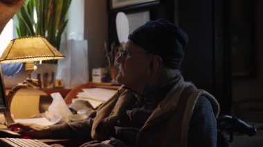 Kronik engelli yaşlı yetişkin tekerlekli sandalyede oturan bilgisayarla çalışıyor.