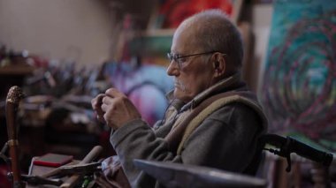 Senior elderly master jeweler in wheelchair works in a workshop with an anvil