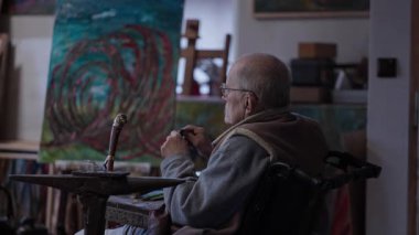 Senior elderly master jeweler in wheelchair works in a workshop with an anvil