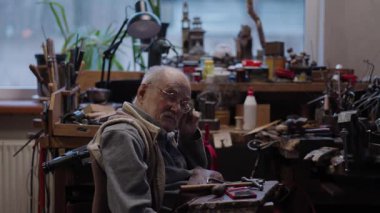 Tekerlekli sandalyedeki kıdemli yaşlı kuyumcu bir atölyede çalışıyor.