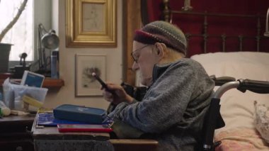 Tekerlekli sandalyedeki yaşlı bir adam yatak odasındaki yatağın yanında ilaç alıyor.