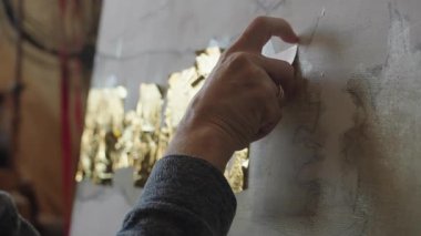 Tekerlekli sandalyedeki kıdemli sanatçı tuvaldeki yağlı boyaya altın sürüyor.