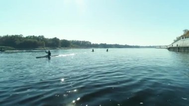 Güneşli bir günde nehir boyunca kürek çeken kürekçiler.