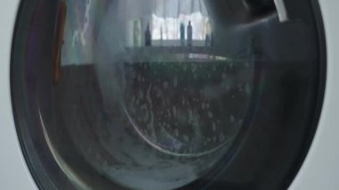 Bulutlu bir günde banyoda pencerenin önünde çamaşır makinesi çalışıyor.