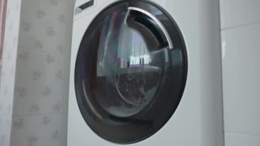 Bulutlu bir günde banyoda pencerenin önünde çamaşır makinesi çalışıyor.