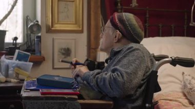 Tekerlekli sandalyedeki yaşlı bir adam yatak odasındaki yatağın yanında ilaç alıyor.