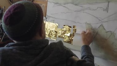 Tekerlekli sandalyedeki kıdemli sanatçı tuvaldeki yağlı boyaya altın sürüyor.