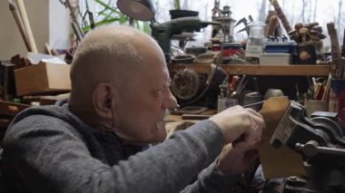 Tekerlekli sandalyedeki kıdemli yaşlı kuyumcu bir atölyede çalışıyor.