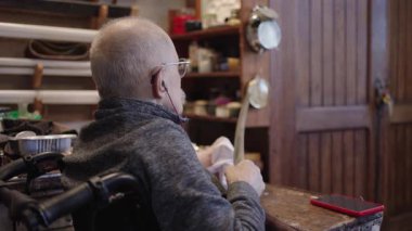 Senior gray haired male master in a wheelchair is working at his workshop sharpening japanese swords blade
